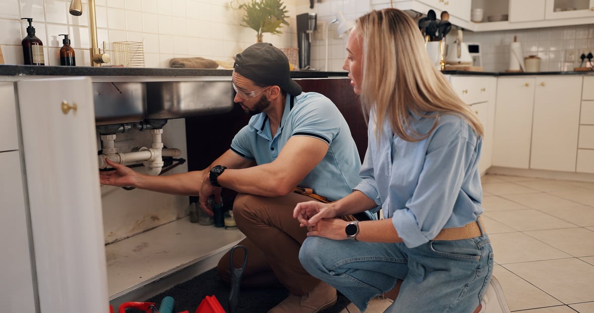 Plumber explaining a leak inspection to a homeowner at the kitchen sink
